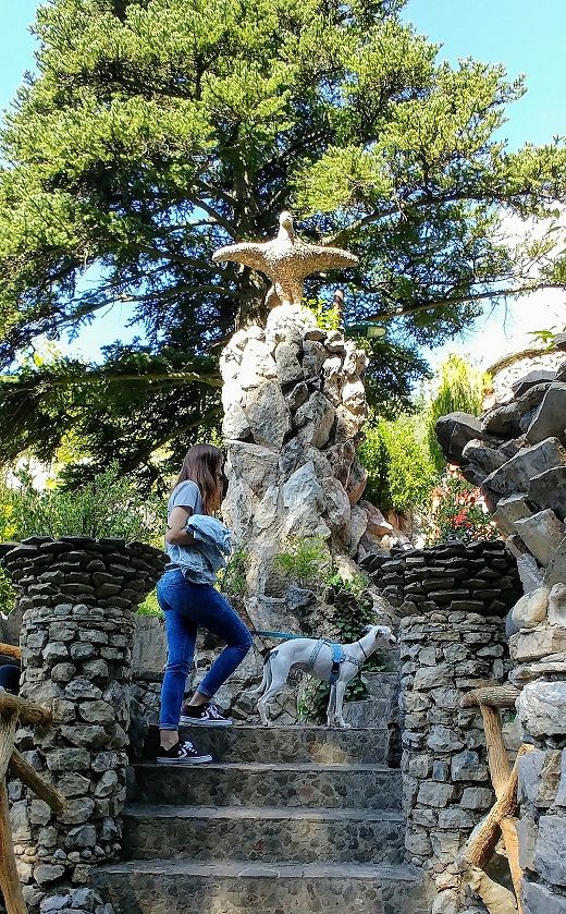 Imagen de diversas columnas cilindricas y hechas de piedra, la más alta coronado por un aguila, una chica con perro, es un tramo de la escalera de los jardins Artigues, la primera parada del tren del ciment