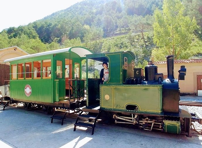 Maquina de tren a la que se puede subir en el museu del ciment, un niño conduciendo en su interior, alfondo los paisajes naturales del bergueda. Es el final del recorrido del tren del ciment