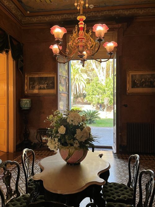 Qué evre en las salas Nobles del Palau Mercader. Estancia con una mesa y flores y vistas al parque